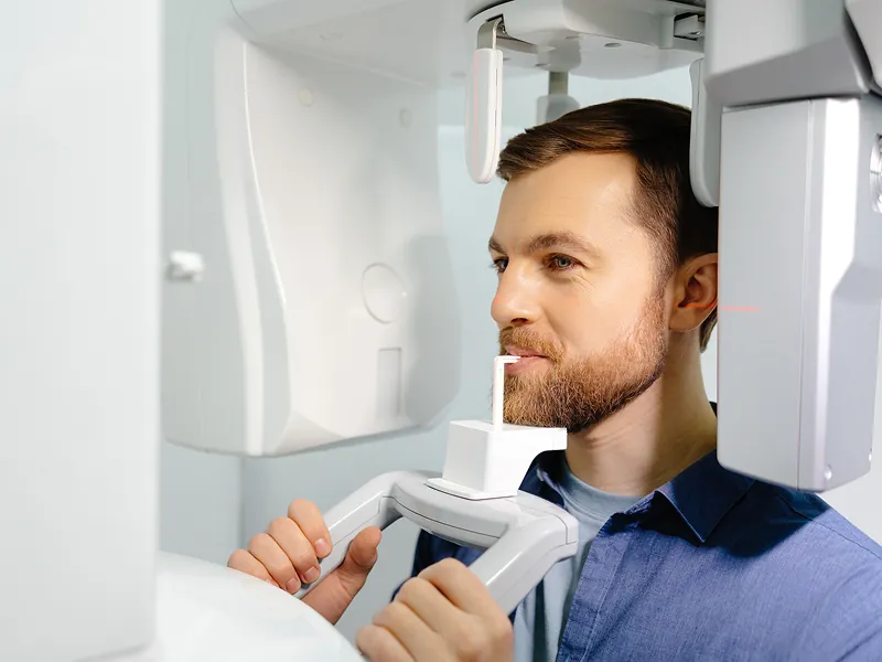 Man undergoing dental panoramic X-ray scan in a bright, modern clinic. Focus on professional medical diagnostic imaging equipment and patient.